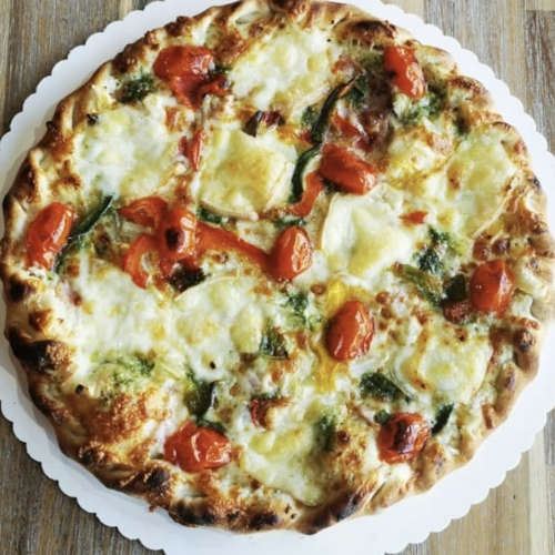 pizza-audacieuse photo du dessus d'une pizza audacieuse composée de crème, jambon, oignons, beurre persillé, raclette, poivrons, tomate cerise, fromage